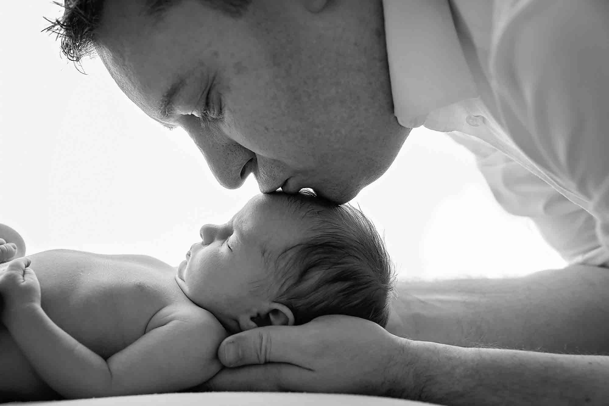 dad kissing newborn baby on forehead